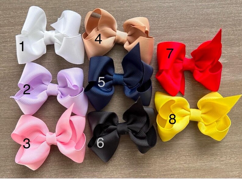 May include: Eight different colored hair bows with numbers 1 through 8 on them. The bows are made of a soft, textured fabric and are arranged in a row.