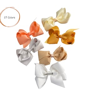 May include: Six different colored hair bows with a white background. The bows are made of satin ribbon and are tied with a knot in the center. The text "27 Colors" is written in a circle above the bows.