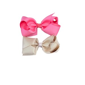 May include: Two hair bows, one pink and one beige, tied together with a white ribbon.