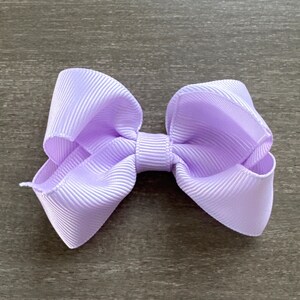 May include: A lavender-colored hair bow with a simple, classic design. The bow is made of a soft, textured fabric and is perfect for adding a touch of elegance to any outfit.