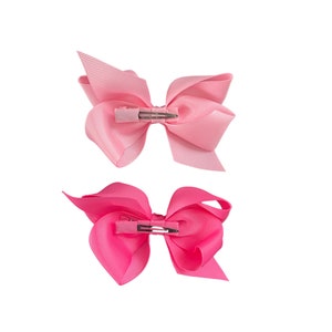 May include: Two pink hair bows with alligator clips. The top bow is a light pink and the bottom bow is a hot pink.