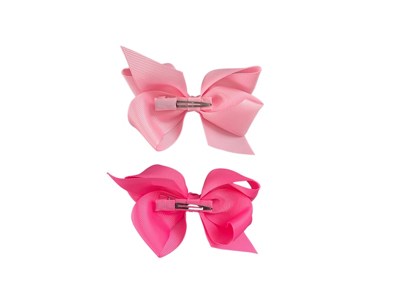 May include: Two pink hair bows with alligator clips. The top bow is a light pink and the bottom bow is a hot pink.