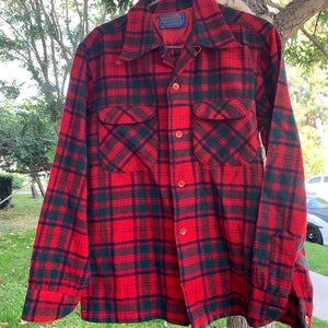 May include: Red and black plaid flannel shirt with a button-up front and two chest pockets. The shirt has a label that reads "Woolrich, Woolrich, Inc., New York, N.Y."