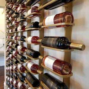 May include: A wall-mounted wine rack featuring a gold-toned metal frame with multiple horizontal cradles. Each cradle holds a single glass wine bottle in a horizontal position. The bottles contain various shades of red, rose, and white wine.