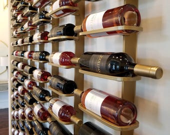 May include: A wall-mounted wine rack featuring a gold-toned metal frame with multiple horizontal cradles. Each cradle holds a single glass wine bottle in a horizontal position. The bottles contain various shades of red, rose, and white wine.
