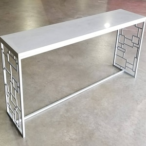May include: White console table with a geometric metal frame. The table has a white top and a white metal base with a geometric design.