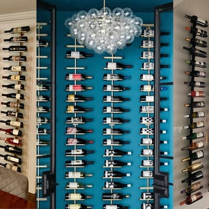 May include: Three different wall-mounted wine racks with bottles of wine. The racks are made of metal and have a modern design. The wine bottles are arranged in rows and are of various colours and labels.