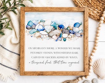 May include: A square wooden framed sign featuring a watercolor illustration of blue, white, and grey stones along a shoreline. The text reads: ON MICHIGAN'S SHORE, A WONDER WE SHARE PETOSKEY STONES, WITH PATTERNS RARE, CARVED BY GLACIERS, KISSED BY WAVES, a treasured find, that time engraved.