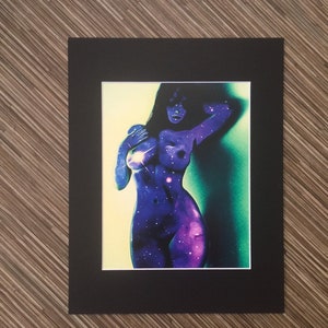 May include: A black framed print of a woman with a galaxy-like pattern on her body. The background is a gradient of yellow, green, and blue.