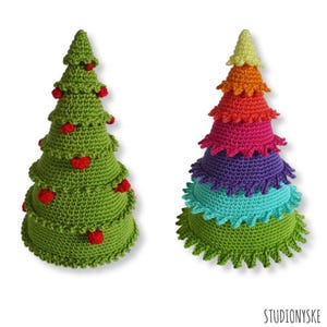 Puede incluir: Dos árboles de Navidad de crochet. Uno es verde con adornos rojos y el otro está en capas con colores arcoíris.