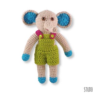 May include: A crocheted elephant toy wearing green dungarees with pink and yellow buttons. The elephant has blue ears and a brown nose.