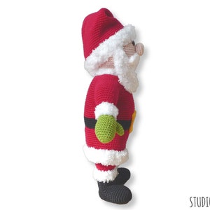 May include: A crocheted Santa Claus doll with a red suit, white trim, and a green mitten. The doll is standing on a white background.