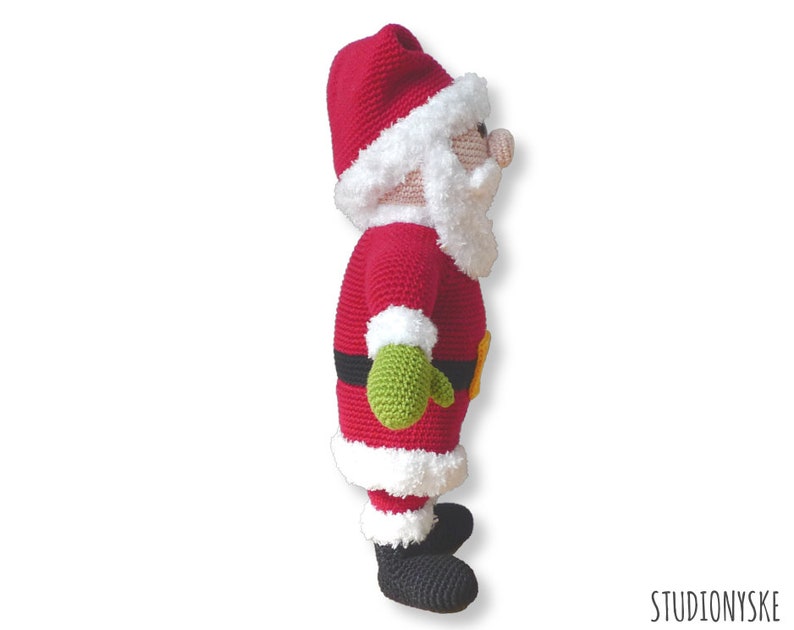 May include: A crocheted Santa Claus doll with a red suit, white trim, and a green mitten. The doll is standing on a white background.