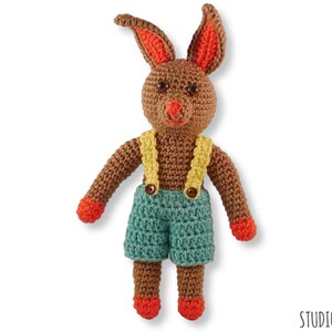 May include: A brown crocheted bunny wearing blue dungarees with yellow straps and orange shoes.