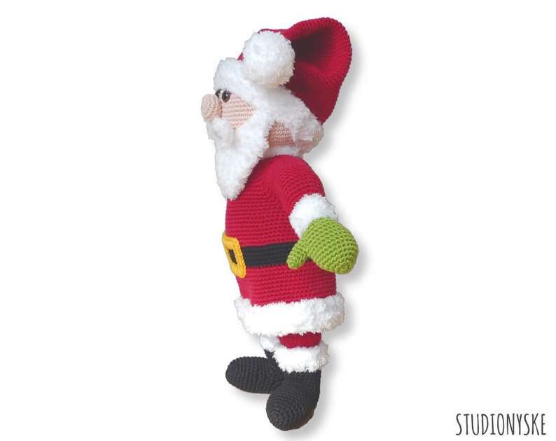 May include: A crocheted Santa Claus doll with a red suit, white beard, and black boots. The doll is wearing a green mitten on one hand and has a black belt with a yellow buckle.