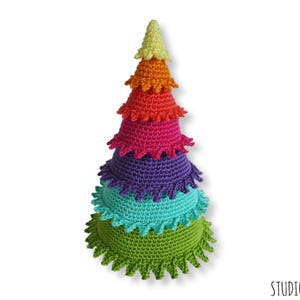 Puede incluir: Un juguete de &aacute;rbol de Navidad de crochet de color arco&iacute;ris con una base verde, una capa turquesa, una capa morada, una capa roja, una capa naranja y una parte superior amarilla.
