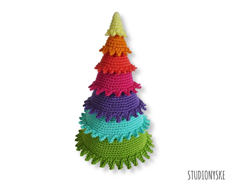 Puede incluir: Un juguete de &aacute;rbol de Navidad de crochet de color arco&iacute;ris con una base verde, una capa turquesa, una capa morada, una capa roja, una capa naranja y una parte superior amarilla.