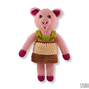 May include: A crocheted pink pig wearing a green, brown and cream dress with pink buttons.