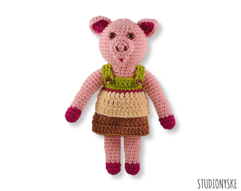 May include: A crocheted pink pig wearing a green, brown and cream dress with pink buttons.