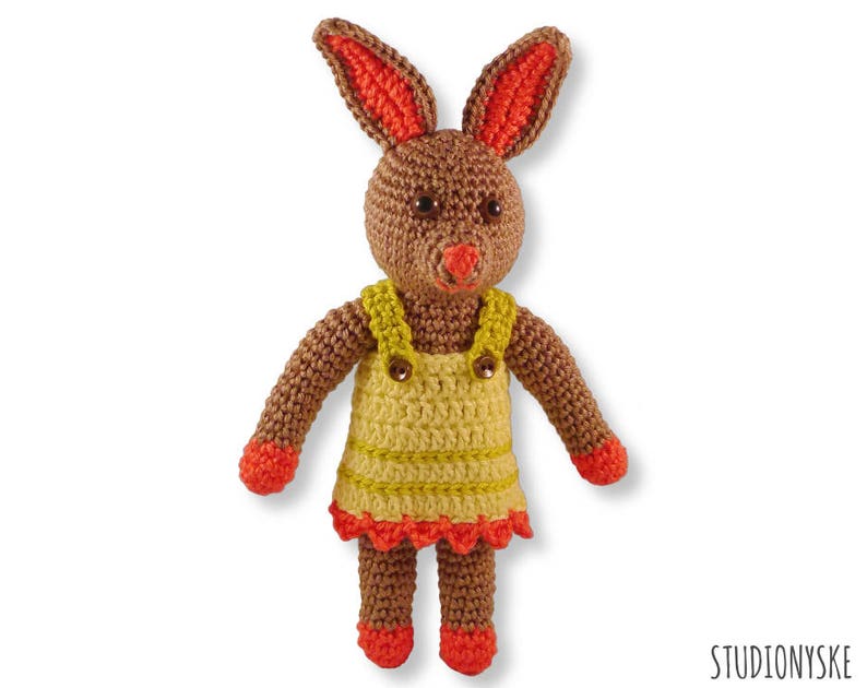 May include: A crocheted brown bunny wearing a yellow and orange dress with a crocheted flower detail.