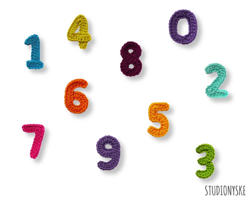 May include: Crocheted numbers 0 through 9 in various colors. The numbers are arranged in a random pattern on a white background.