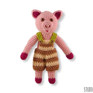 May include: A pink crocheted pig wearing brown and cream striped dungarees with green straps. The pig has a pink snout and pink ears.