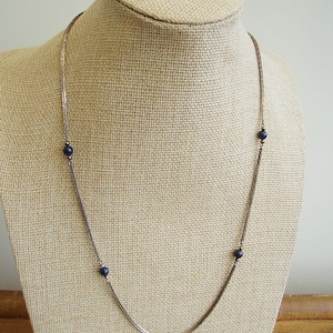 Può includere: Una collana a catena d'argento con quattro perle rotonde blu scuro.