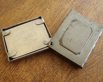 May include: A vintage metal cigarette case with a hinged lid. The case is engraved with the text "MADE BY MIDLAND SUPPLY CO."