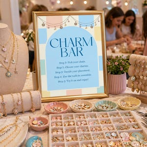 Peut inclure: Un atelier de création de bijoux avec une enseigne "Charm Bar". Des colliers, des bracelets et divers charms de différentes couleurs et formes sont exposés. Des outils et des petits plats de charms sont également visibles.