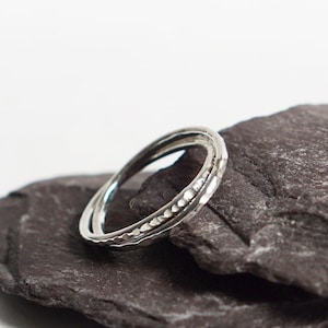 May include: A silver ring with a textured band, resting on a dark gray stone.