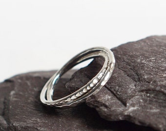 Puede incluir: Un anillo de plata con una banda texturizada, descansando sobre una piedra gris oscura.