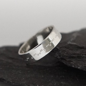 May include: A silver ring with a band of raised dots, set on two pieces of dark grey slate.