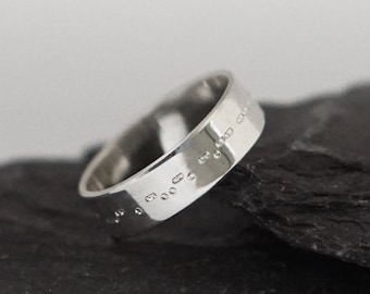 May include: A silver ring with a band of raised dots, set on two pieces of dark gray slate.