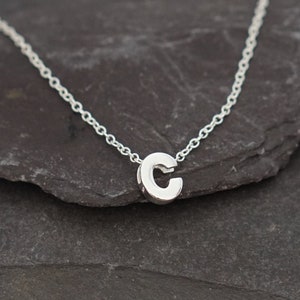 May include: A silver chain necklace with a small, silver letter 'C' pendant.
