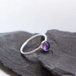 May include: A silver ring with a small, round, purple amethyst gemstone.
