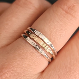 May include: Three silver rings stacked on a finger. The top ring says "BESTIE" in gold lettering. The middle ring says "GOOD VIBES" in gold lettering. The bottom ring says "JUST BREATHE" in silver lettering.