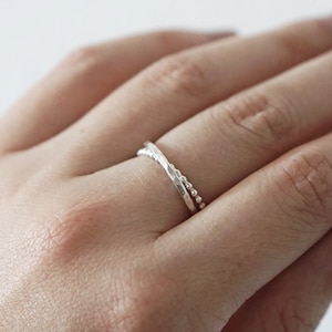 May include: A silver ring with a twisted design. The ring is worn on the ring finger of a hand.