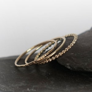 May include: Set of four gold stacking rings. The rings are thin and delicate, with a variety of textures. The rings are stacked on top of each other, creating a layered look.