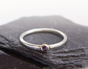 Puede incluir: Un anillo de plata con una banda texturizada y una pequeña piedra preciosa púrpura engastada en un engaste de oro.