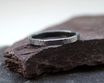 Op de afbeelding: Een zilveren ring met een getextureerde, gehamerde afwerking. De ring ligt op een donkergrijze leisteen.