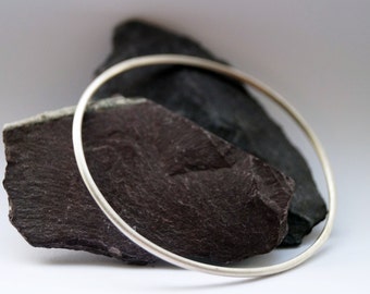 May include: A silver bangle bracelet resting on two dark gray slate stones.