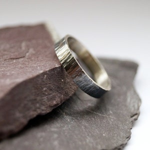 May include: A silver ring with a textured, hammered finish. The ring is resting on two pieces of slate.