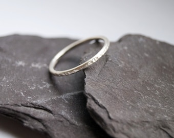 May include: A simple silver band ring with a textured finish. The ring is displayed on a dark gray slate surface.