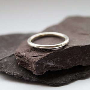 May include: A simple silver band ring resting on two pieces of dark gray slate.