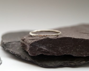 May include: A thin silver ring with a textured surface, resting on a dark gray stone.
