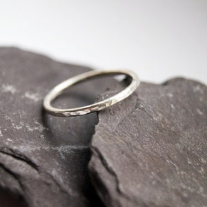 May include: A thin silver band ring with a hammered texture. The ring is resting on two pieces of dark gray slate.
