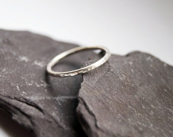 May include: A thin silver band ring with a hammered texture. The ring is resting on two pieces of dark gray slate.