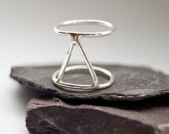 May include: A silver ring with a geometric design featuring a triangle and a circle.