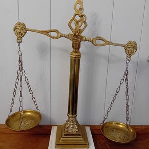 May include: A gold-tone decorative scale with a marble base. The scale has two hanging pans and a central column with an ornate design. The scale is a decorative piece and not intended for use.