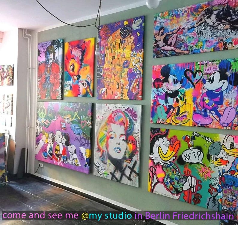 May include: A collection of vibrant pop art canvases displayed on a wall, featuring iconic characters like Mickey Mouse, Donald Duck, the Joker, and Marilyn Monroe, alongside stylized interpretations of famous paintings with graffiti-style paint splatters.